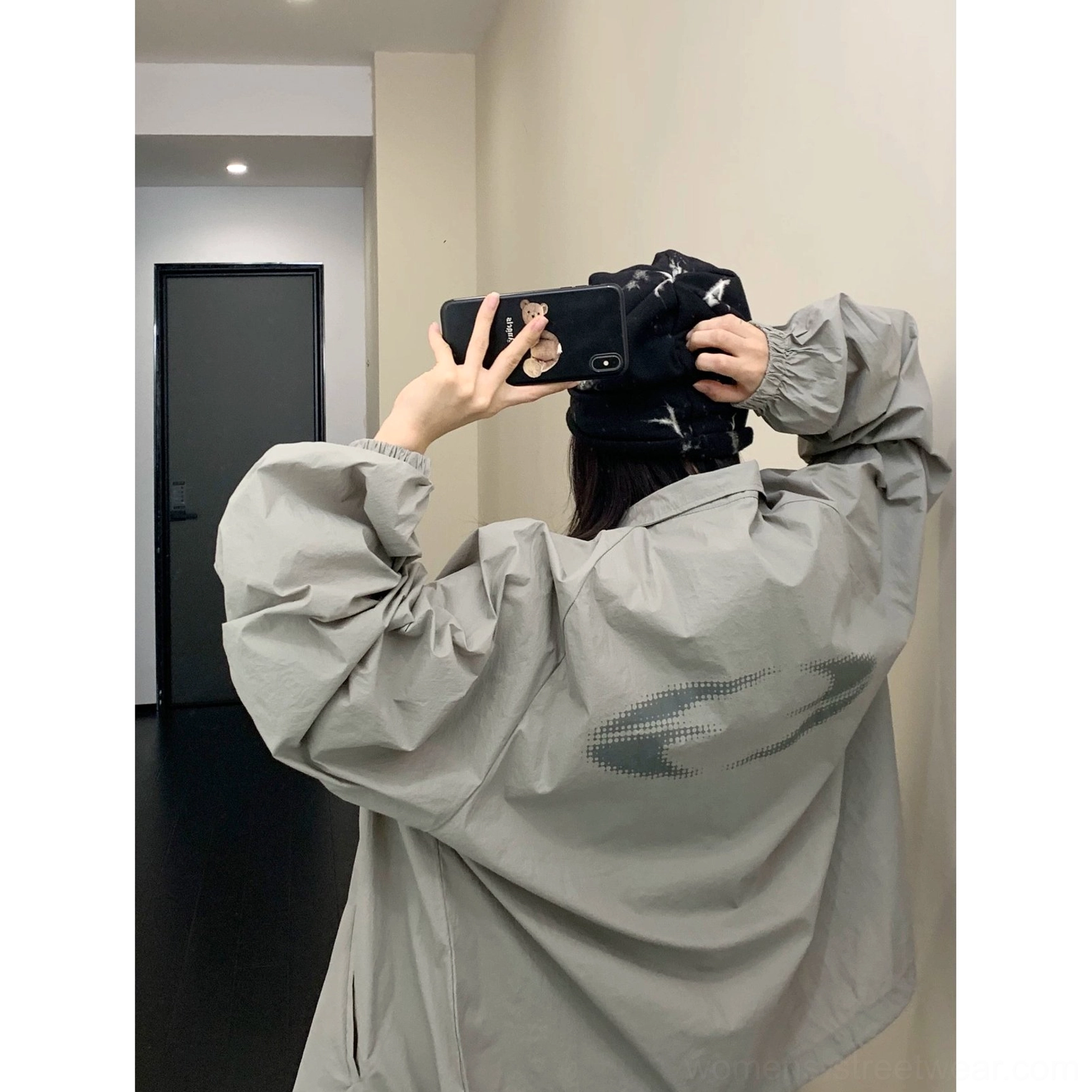 Back mirror view of an oversized gray UPF50+ windbreaker jacket worn with a black baseball cap, showing the loose silhouette, long sleeves, and subtle back graphic