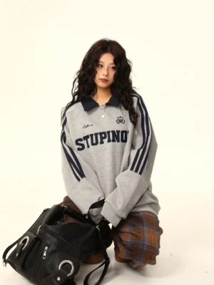 Heather gray oversized varsity polo sweatshirt with navy collar and sleeve stripes styled with plaid wide-leg trousers and a black tote bag