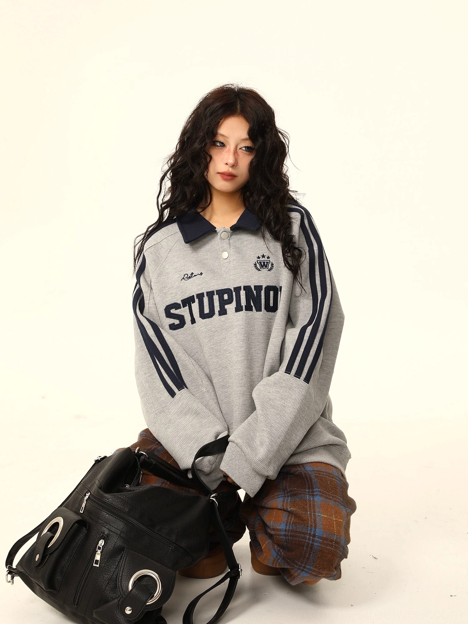 Heather gray oversized varsity polo sweatshirt with navy collar and sleeve stripes styled with plaid wide-leg trousers and a black tote bag