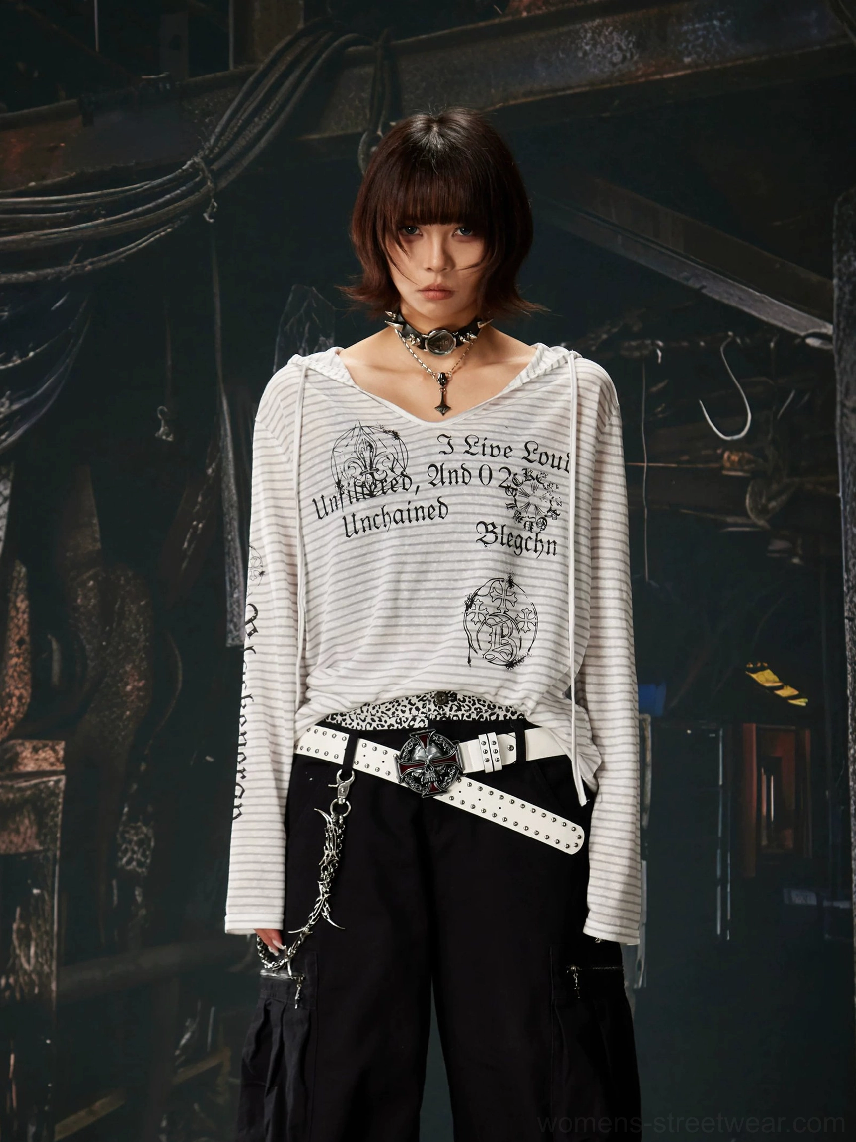 Short-haired model wearing a gray and white striped hooded long sleeve top with the hood down, V-neck detail, gothic graphics, and black cargo pants