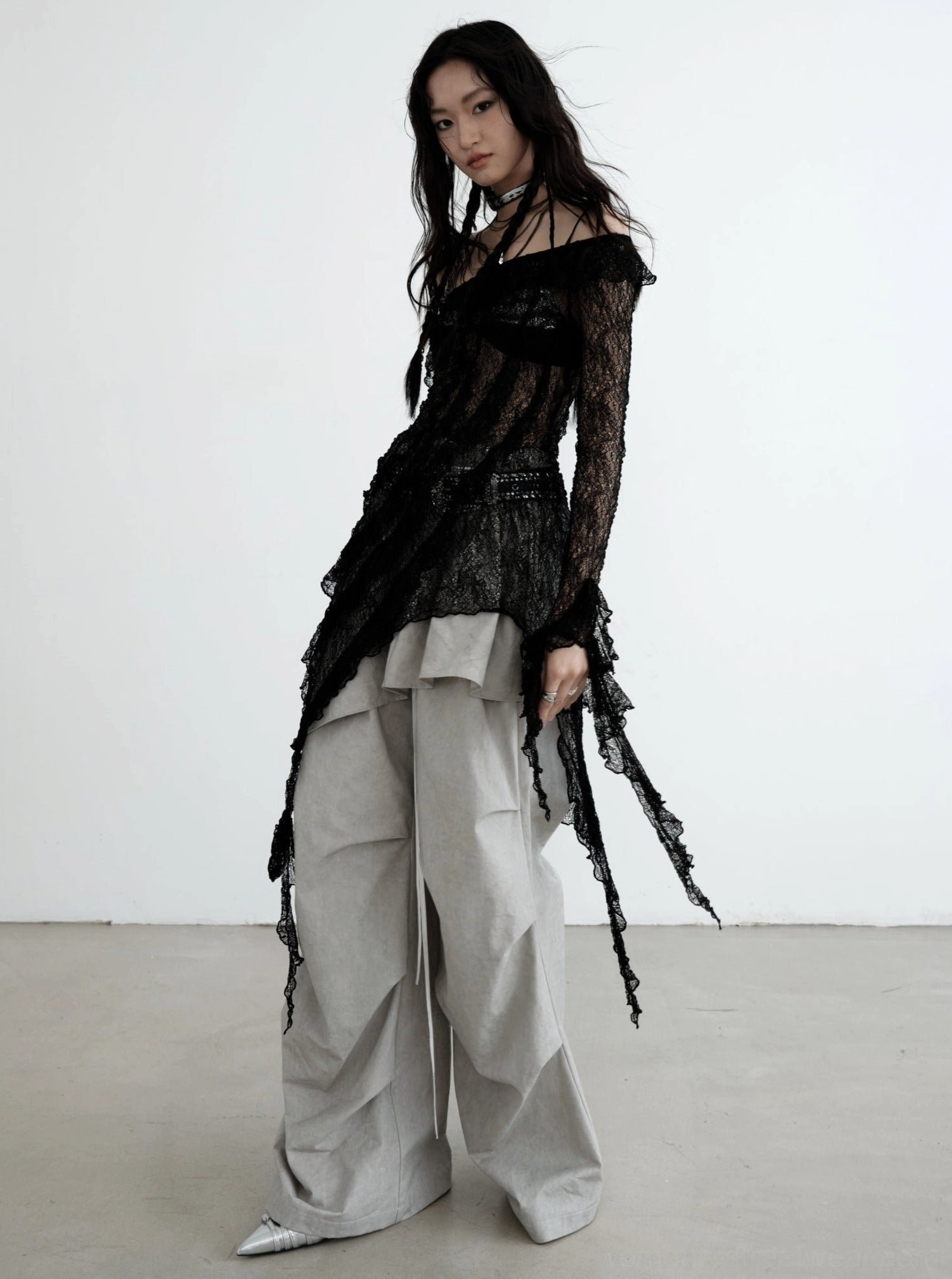 Side view of gray wide-leg cargo pants with drawstring waist styled with an asymmetric sheer lace top for dark Korean streetwear