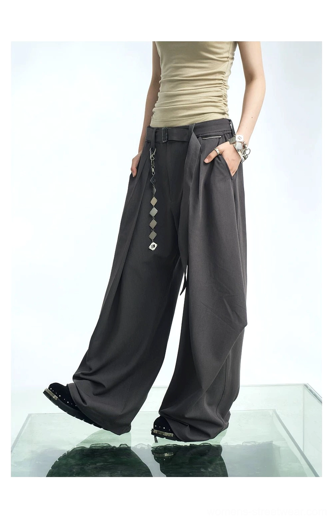 Dark gray wide-leg pleated streetwear pants shown from a three-quarter side angle with a geometric detachable waist chain, flowing balloon legs, cropped top, and platform shoes