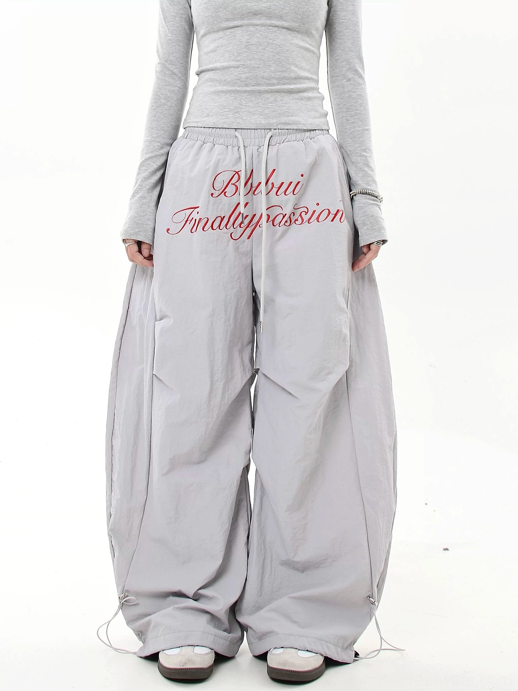 Side-front view of light gray baggy parachute cargo pants with red script embroidery and an extra-wide Korean streetwear silhouette