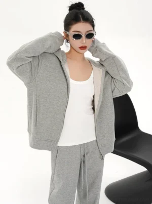 Women's relaxed gray zip-up hoodie jacket worn open over a white tank top in casual Seoul streetwear styling