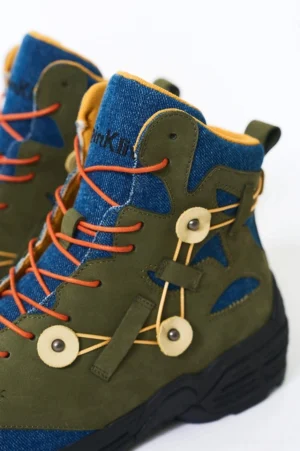 Green denim hiking boots shown from the rear side with decorative buckle straps blue denim ankle collar yellow lining and rugged black outsole