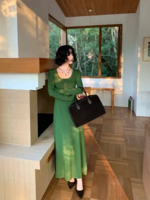 Green fitted ribbed long sleeve maxi dress with wide u-neck shown in a three-quarter side view with a brown leather tote bag