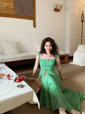 Green floral sleeveless maxi dress with square neckline fitted waist and flowing floor length A-line skirt styled in a vintage indoor setting