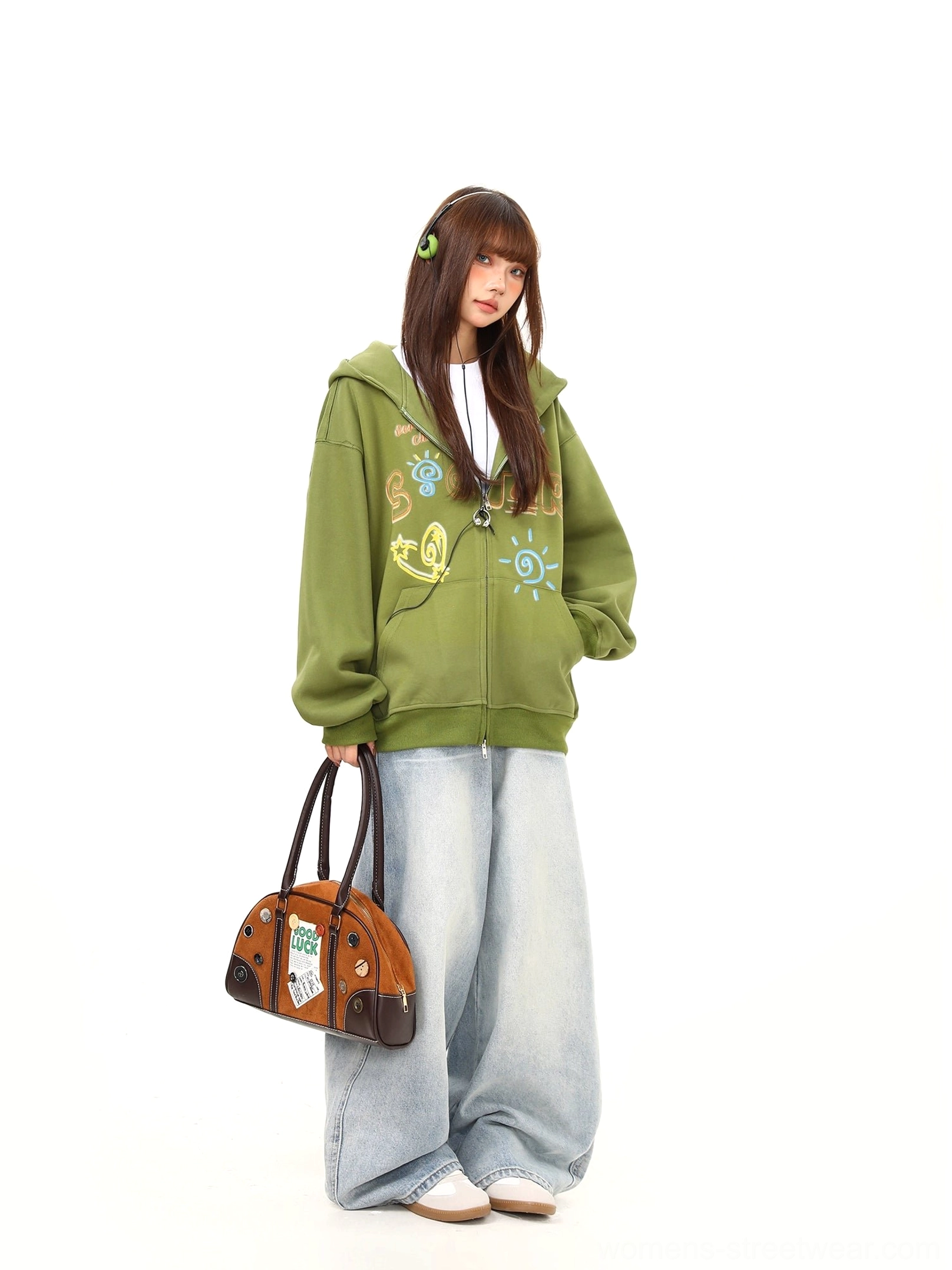 Full-body side view of a relaxed green hooded zip-up hoodie with front doodle graphics styled with wide-leg denim and a handbag
