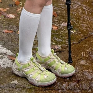 Green and khaki closed-toe mesh hiking sandals with bungee drawcord fastening worn on a wet muddy creek trail