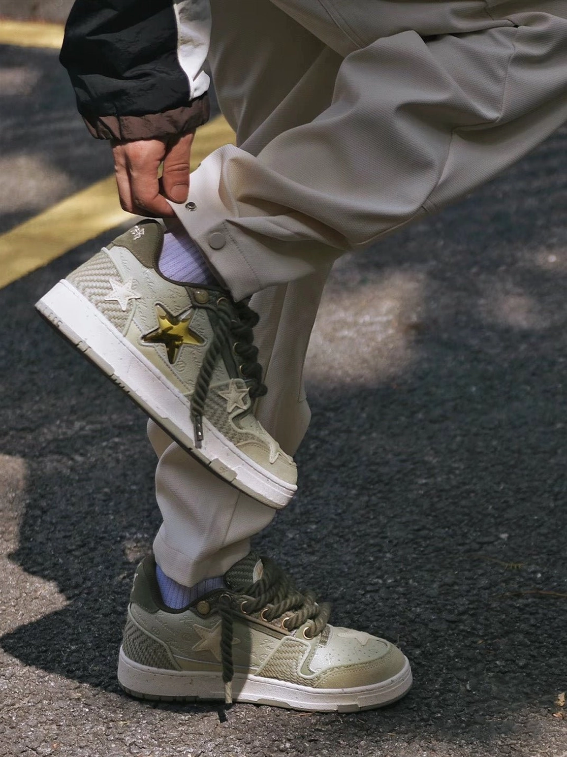 Green Longjing tea star sneakers worn with khaki trousers and black outerwear on an urban street, showing everyday casual streetwear styling