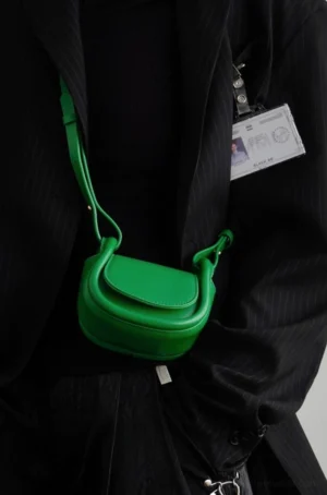Green mini saddle crossbody bag worn with a black tailored suit for colorful Seoul streetwear styling