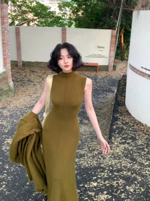 Green raccoon cashmere sleeveless mock neck maxi knit dress worn in an outdoor autumn courtyard with a matching knit layer