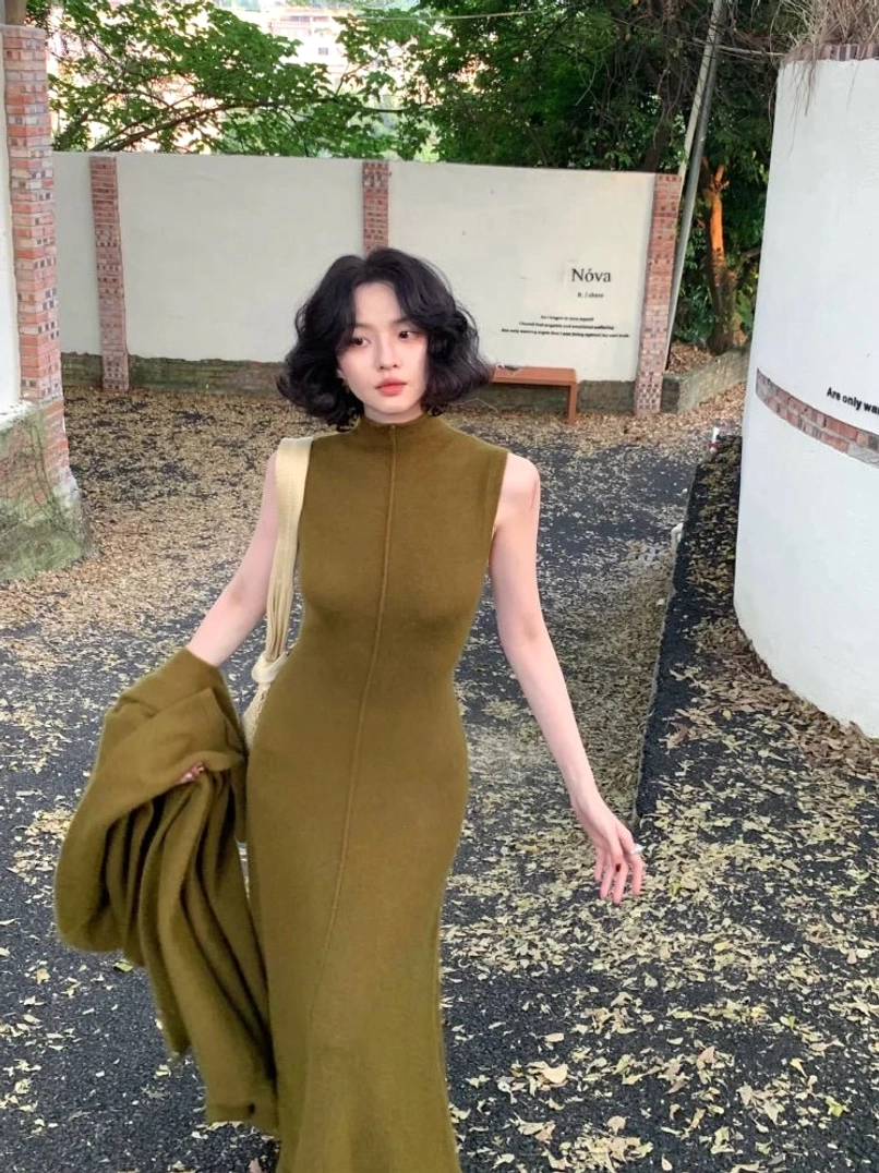 Green raccoon cashmere sleeveless mock neck maxi knit dress worn in an outdoor autumn courtyard with a matching knit layer
