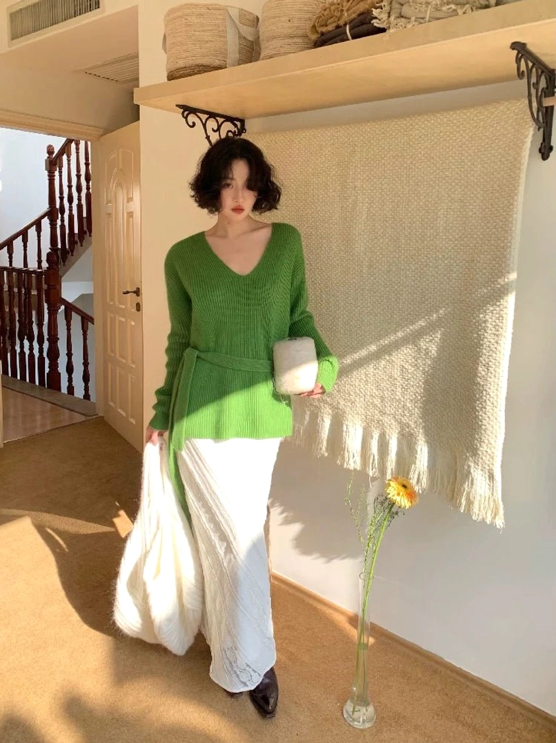 Side view of green ribbed knit V-neck sweater with long scarf tie styled at the waist and white maxi skirt