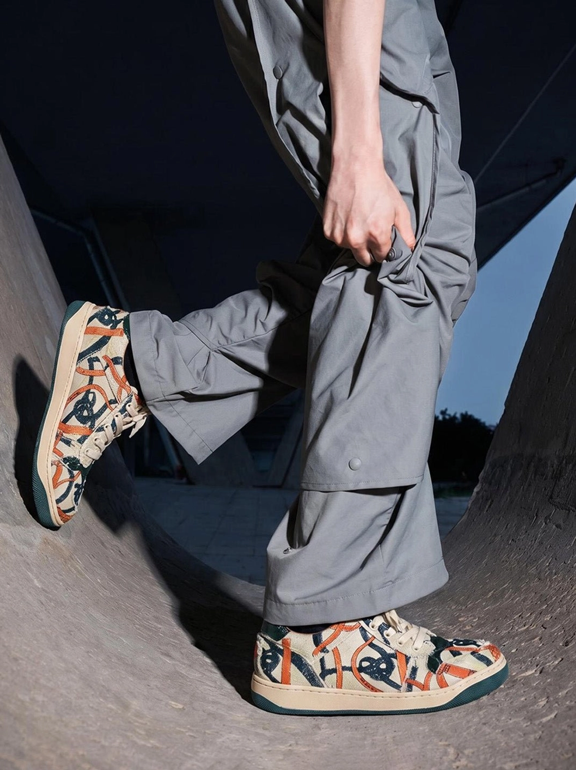 Model wearing green sole graffiti canvas low-top streetwear sneakers with gray cargo pants at a skatepark ramp