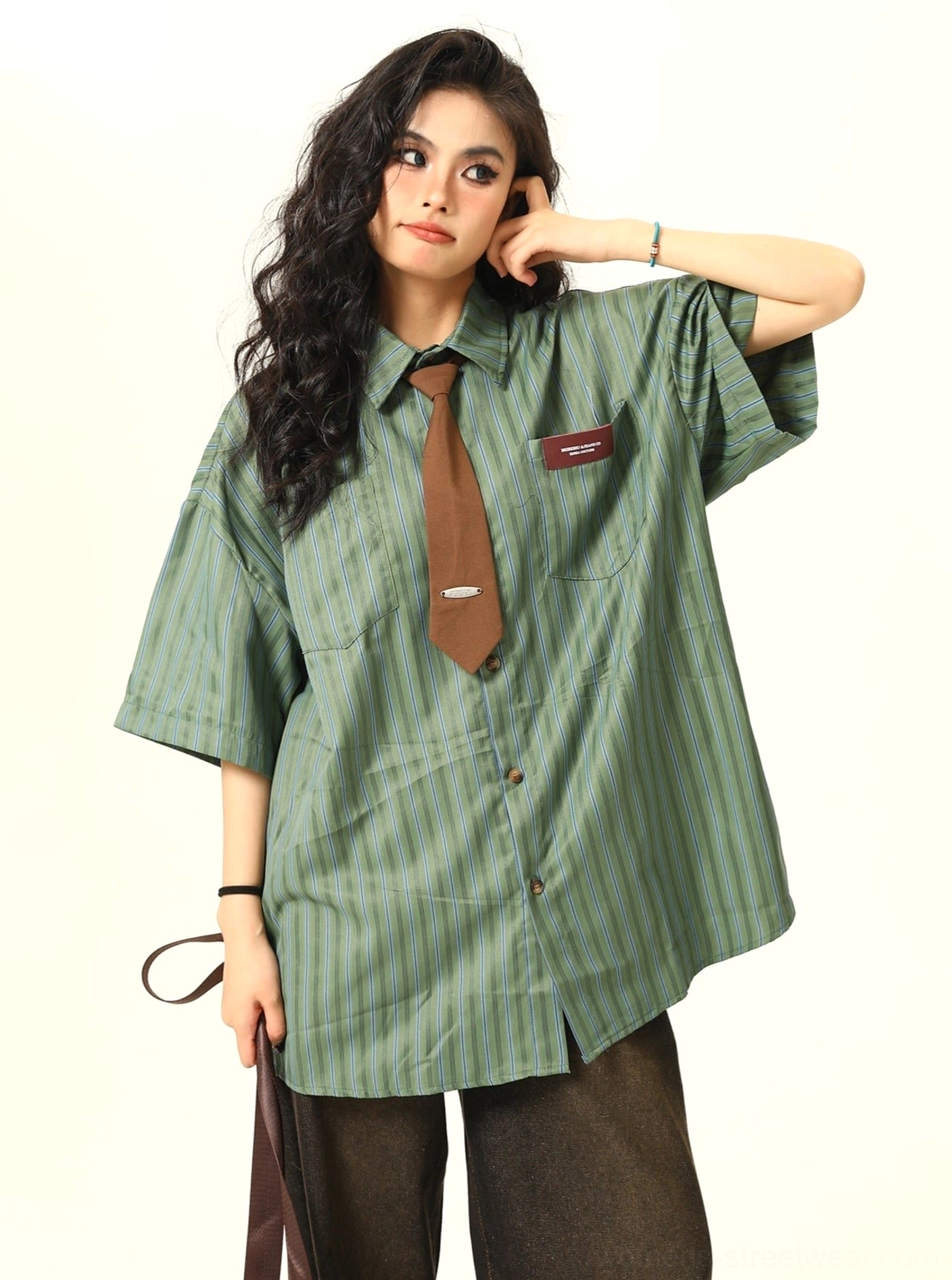 Three quarter view of a green striped oversized button down shirt with short sleeves, side slit hem, chest patch, and brown tie