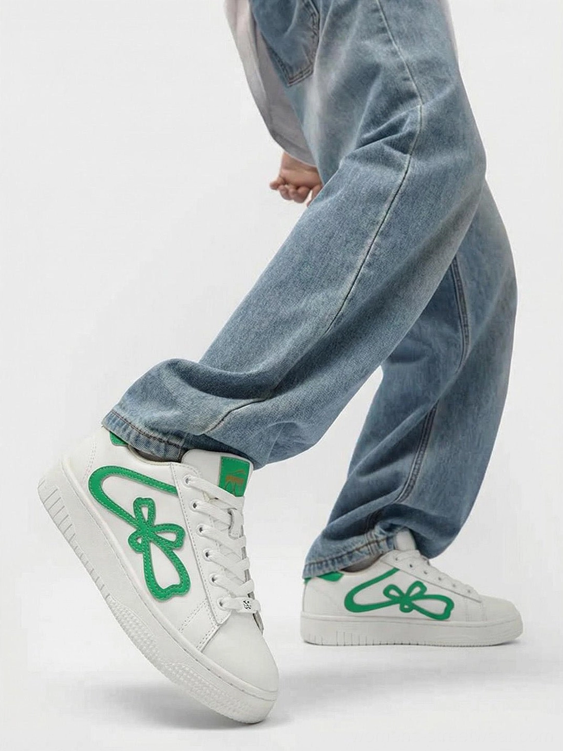 Green and white lucky clover platform sneakers styled on feet with relaxed light blue baggy jeans