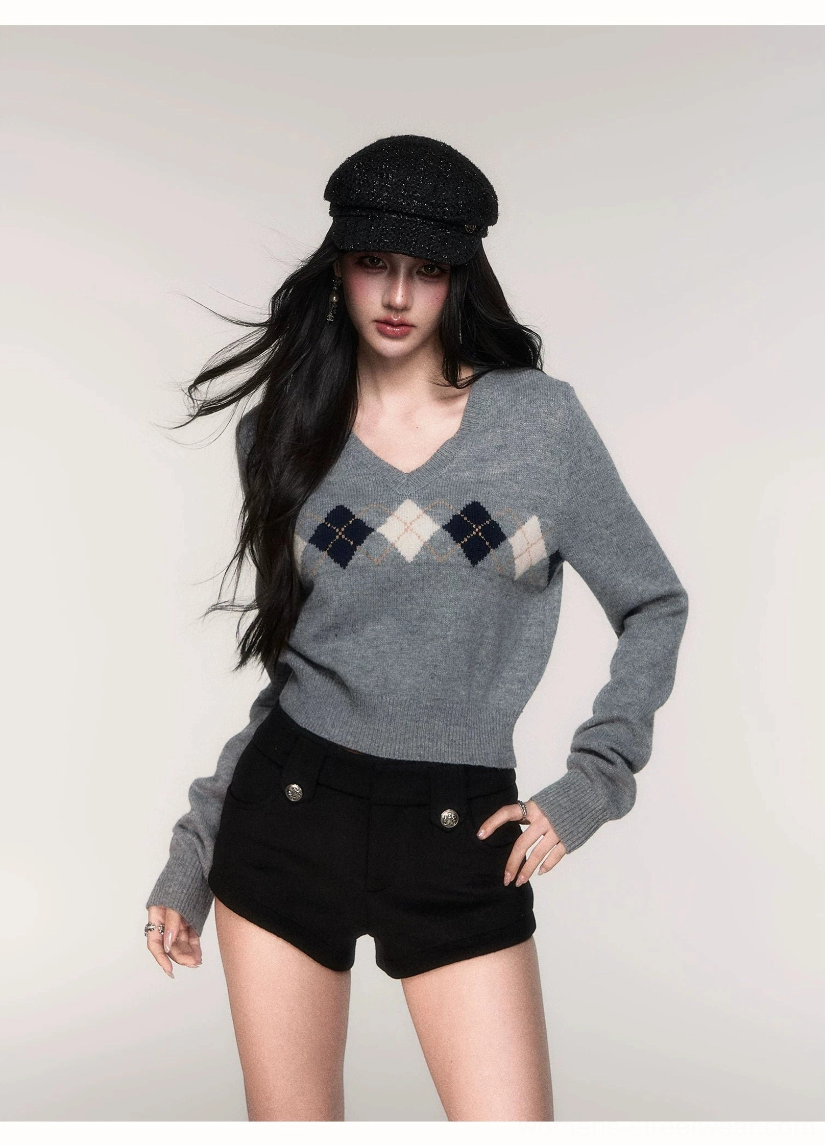 Women's grey argyle cropped V-neck knit sweater in three-quarter front view styled with black tailored shorts and newsboy cap