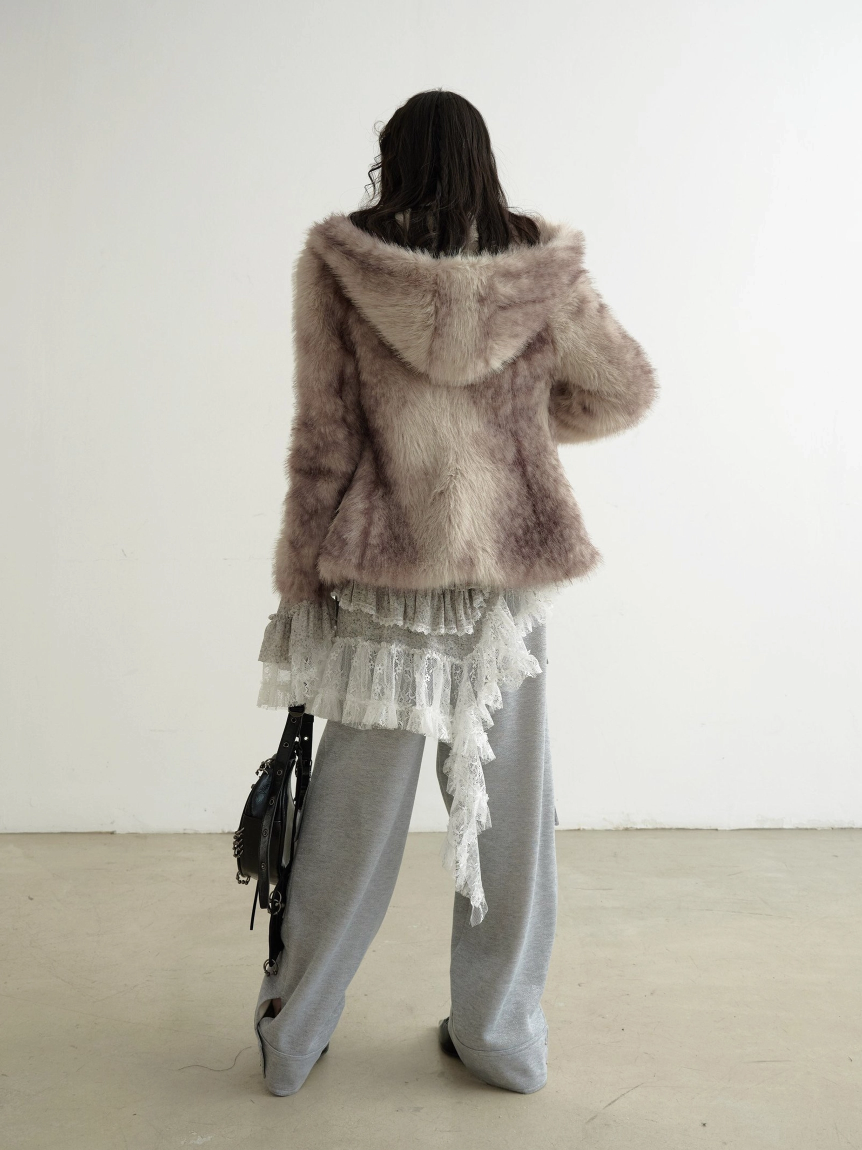 Back view of grey asymmetrical lace knit dress layered under a brown faux fur hooded coat with wide-leg trousers and vintage shoulder bag