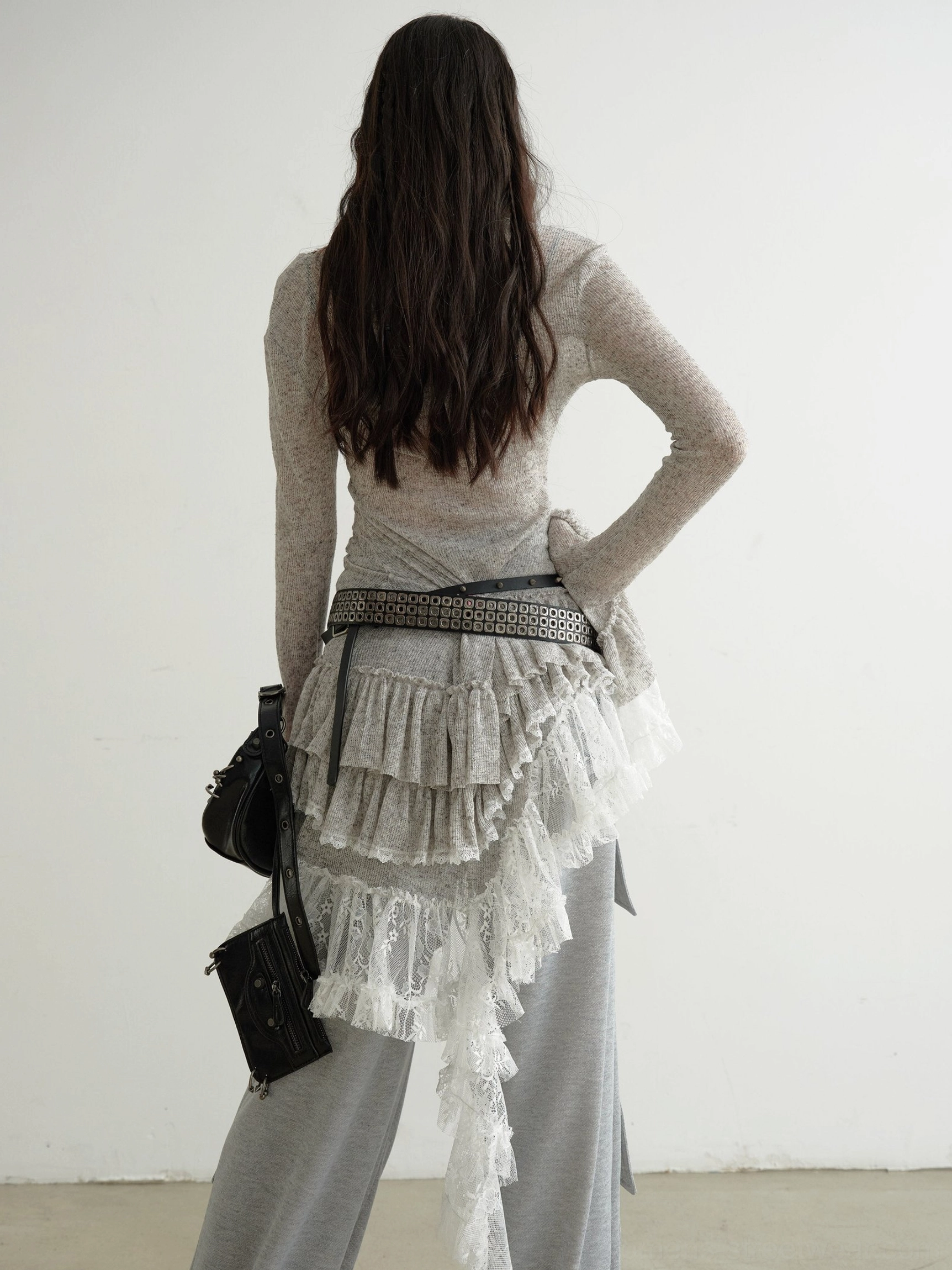 Back view of grey asymmetrical lace panel knit dress showing the flowing ruffle lace train, slim long sleeves, and layered styling with wide-leg trousers