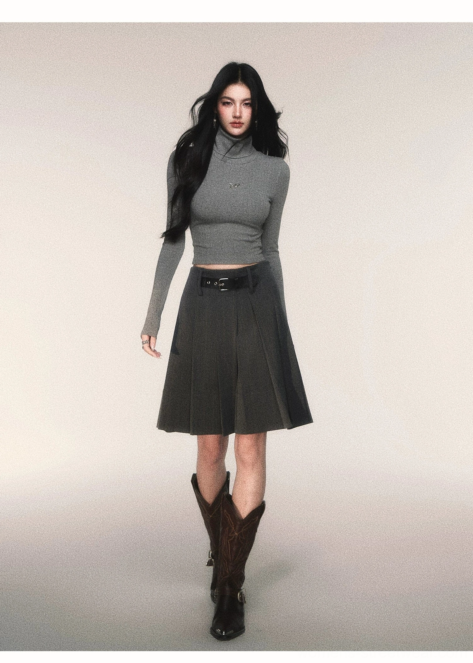 Grey butterfly cropped turtleneck top paired with a belted pleated skirt and brown mid-calf boots