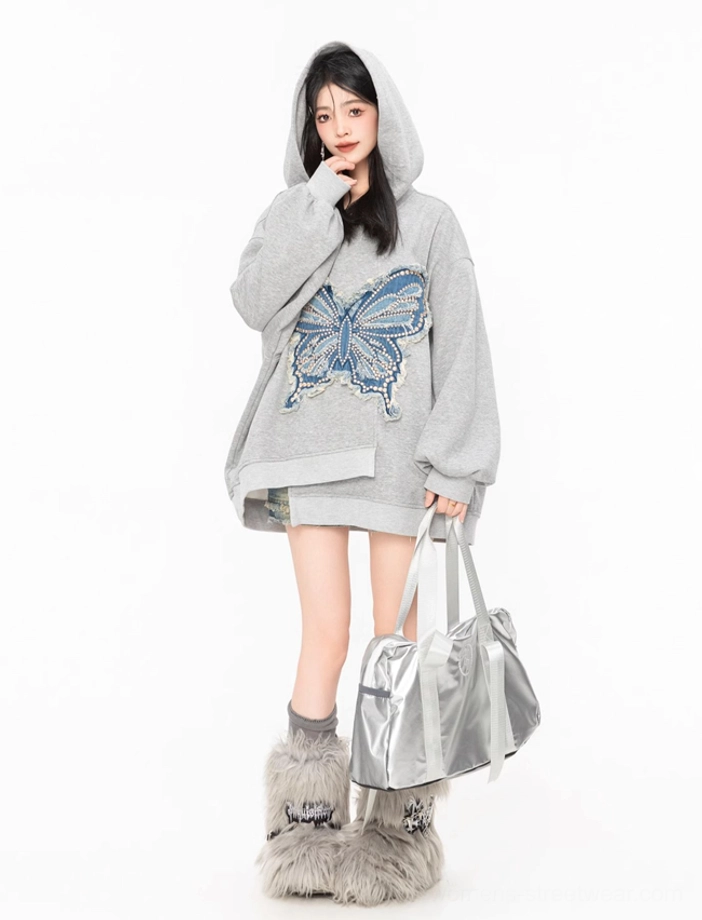Side three-quarter view of a grey butterfly hoodie with hooded neckline, asymmetric hem, and blue frayed denim butterfly appliqué