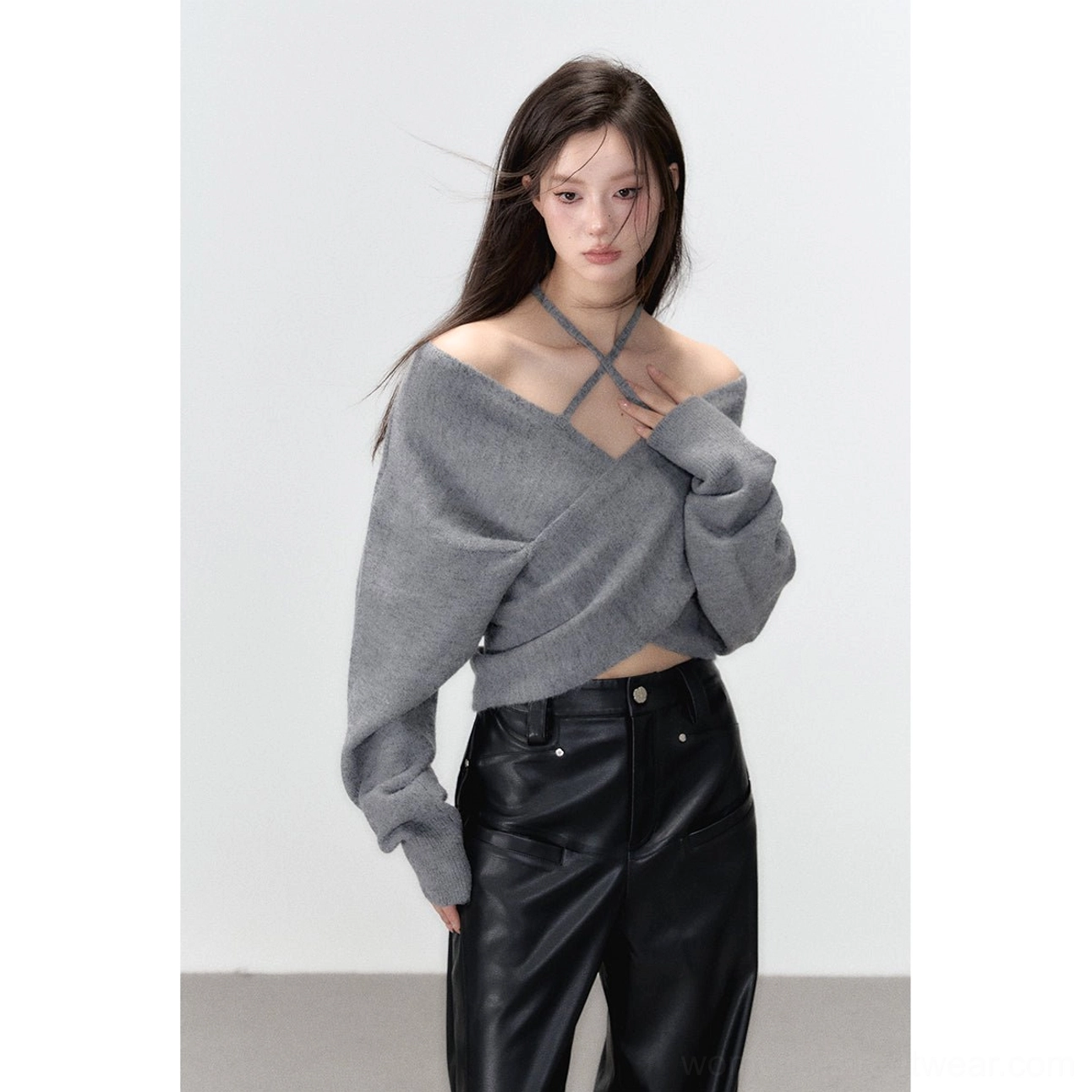 Front medium view of a woman styling a relaxed grey cropped halter knit top with a twisted neckline and black leather streetwear pants