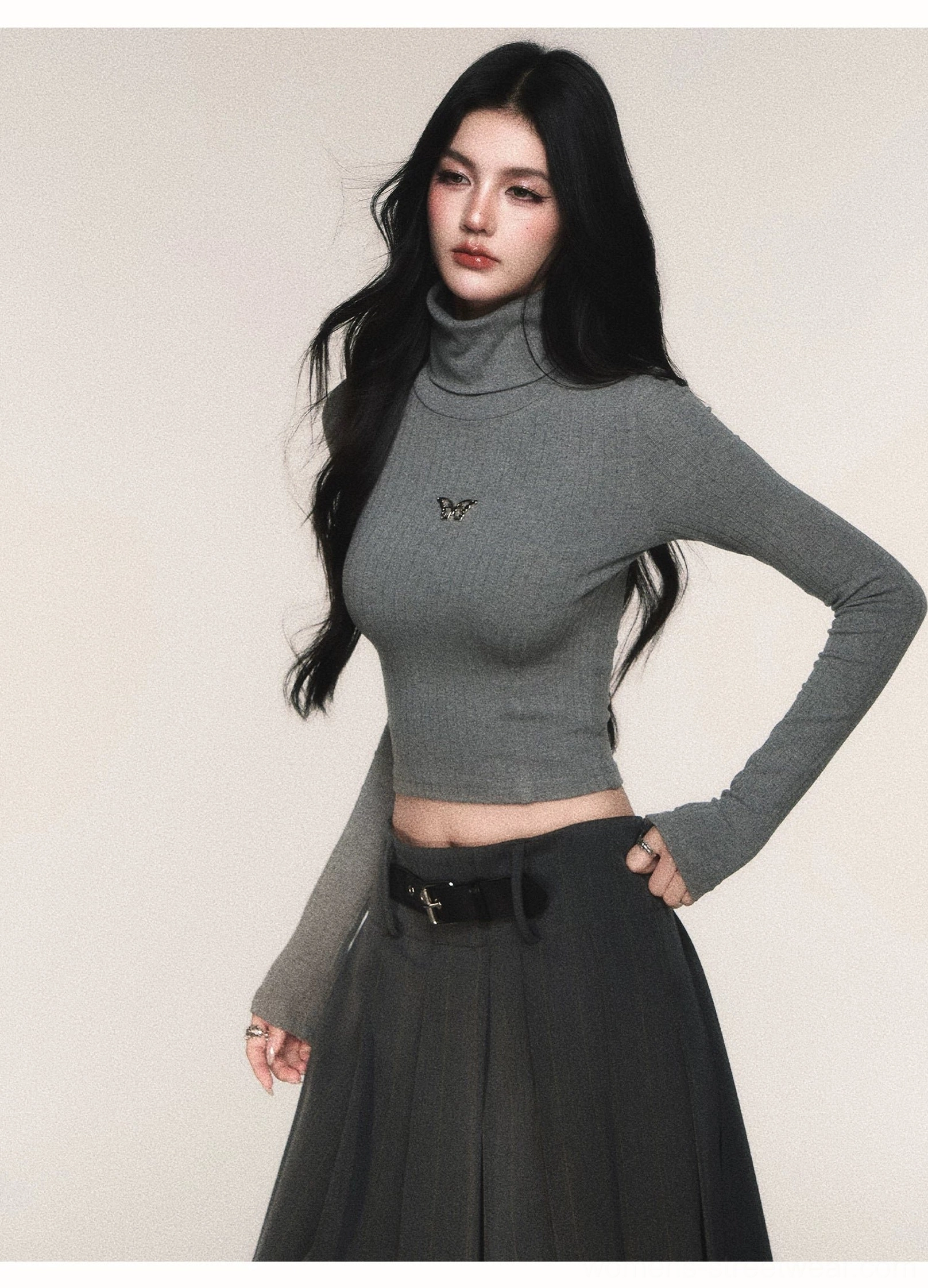Grey cropped turtleneck sweater top with long sleeves and butterfly emblem styled with a belted high-waisted pleated skirt