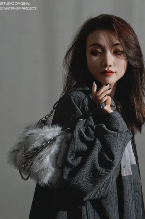 Grey faux fur crescent shoulder bag with silver chain and dark shoulder strap worn by model in side portrait view