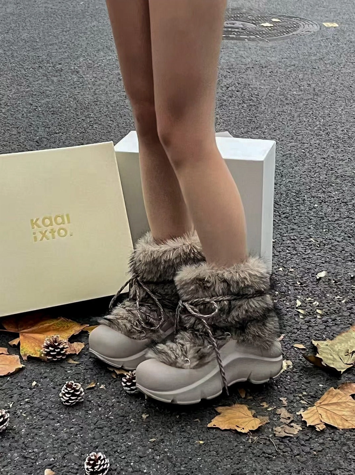 Model wearing grey faux fur platform snow boots outdoors with chunky matte sole and decorative beaded laces