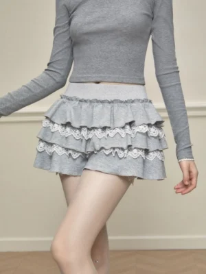 Front close-up of a grey lace trim tiered ruffle skort with high-waisted elastic design and contrasting white lace layers styled with a cropped long-sleeve top