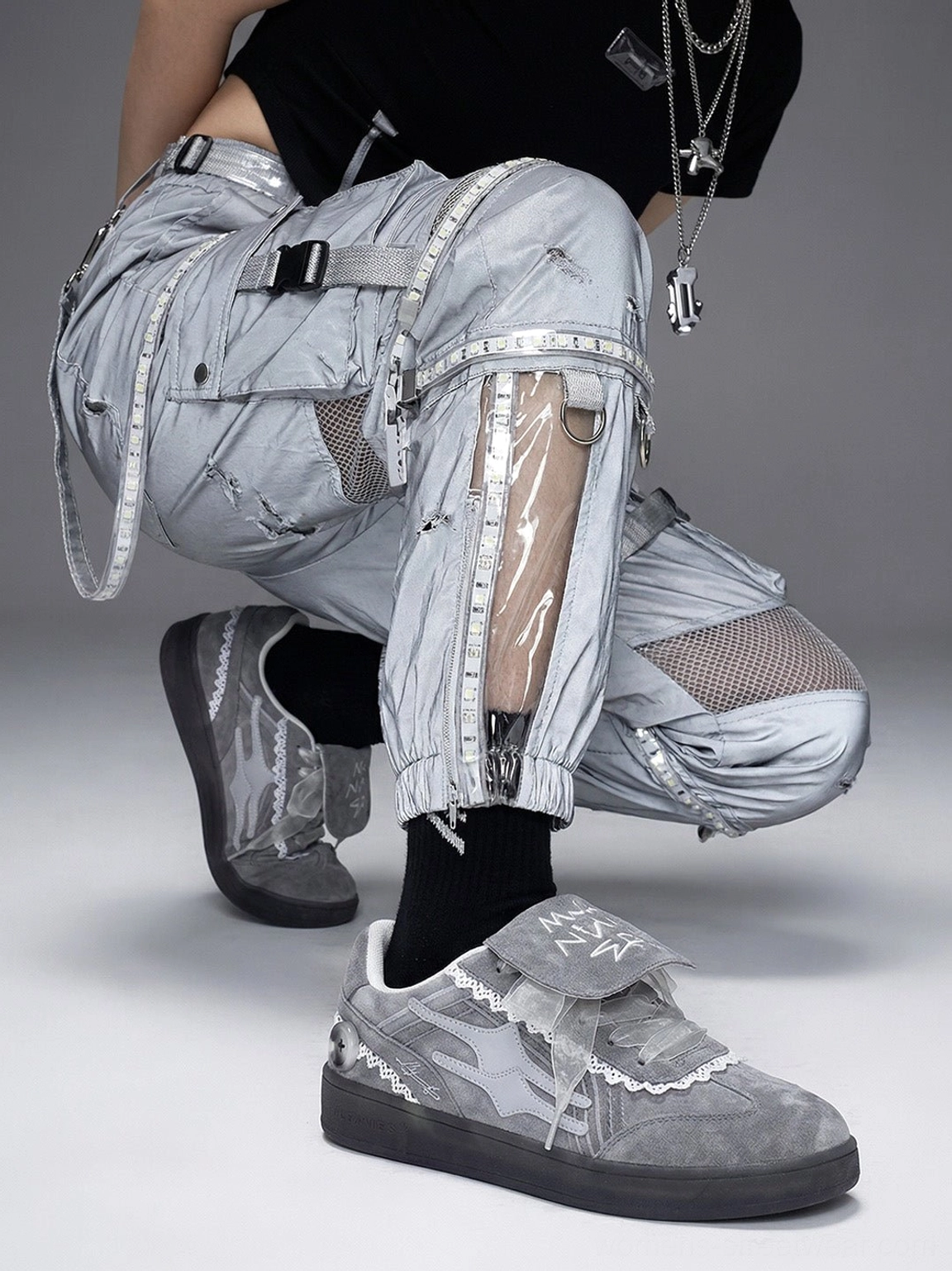 Grey lace-wrapped retro trainer sneakers paired with black tactical mesh cargo pants