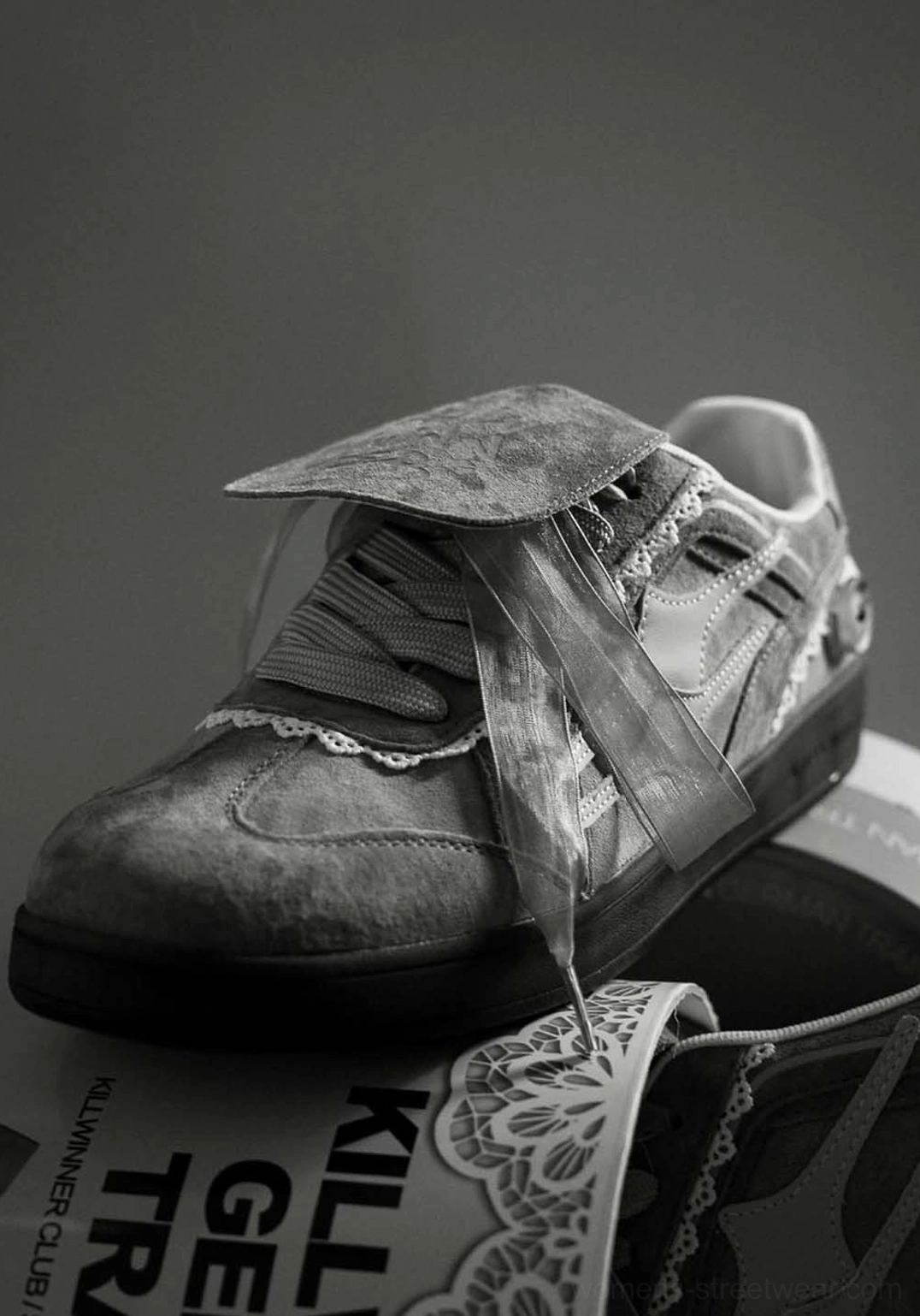 Close-up of grey lace-wrapped retro trainer sneaker with ribbon detail, graffiti flap and textured upper