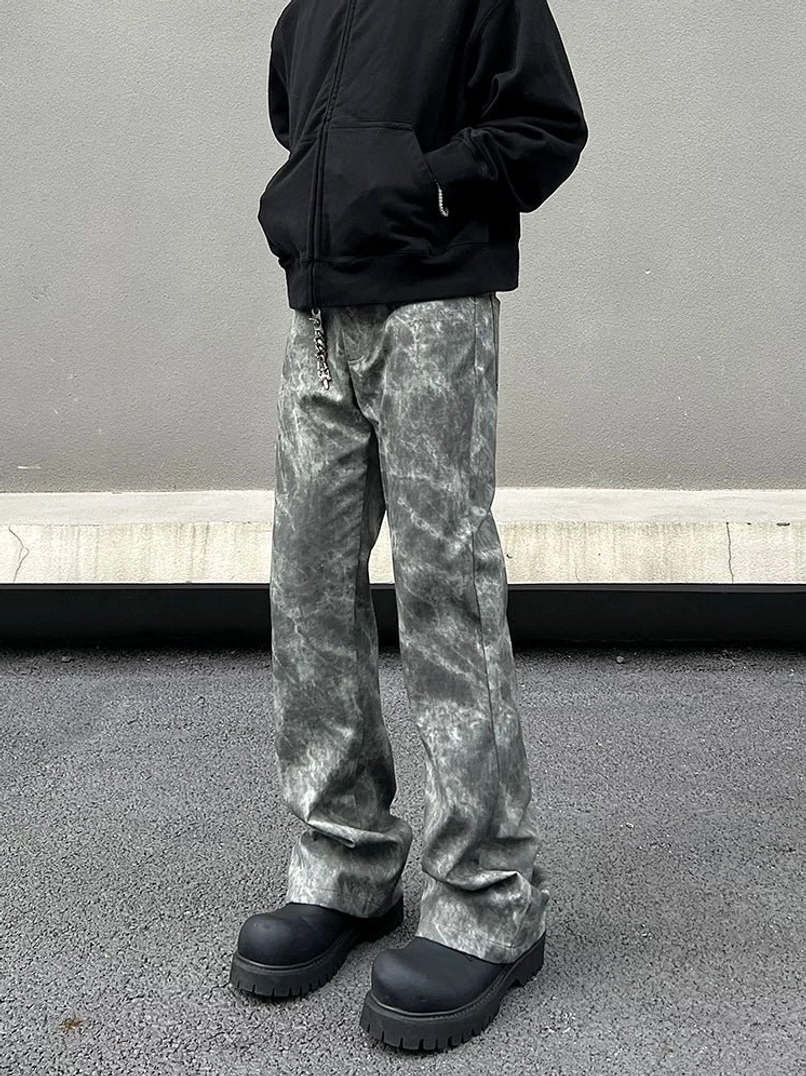 Front low-angle view of grey marble wash relaxed flared streetwear jeans styled with a black zip-up hoodie and black platform shoes