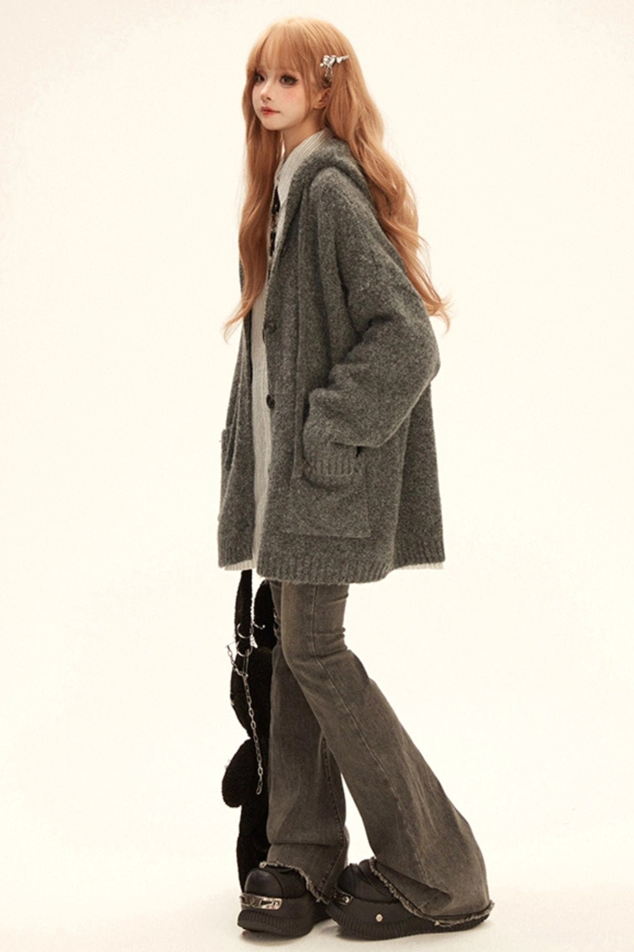 Side view of grey oversized hooded knit cardigan coat with hands in patch pockets and platform shoe styling