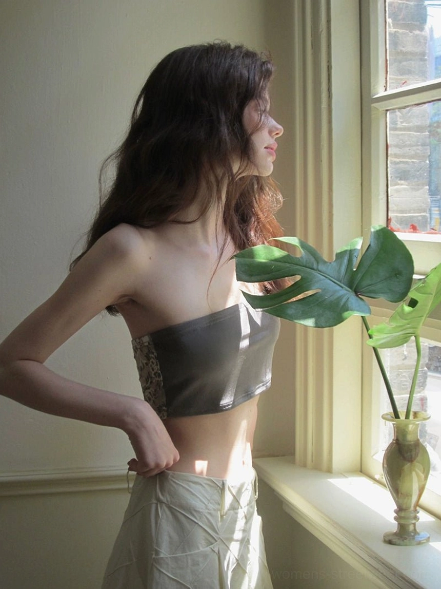 Solid grey strapless cropped bandeau top with exposed waist styled with a khaki midi skirt beside a potted plant