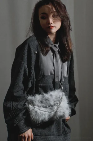 Grey spotted faux fur chain shoulder bag worn with a dark grey textured coat in a minimalist studio front three-quarter view