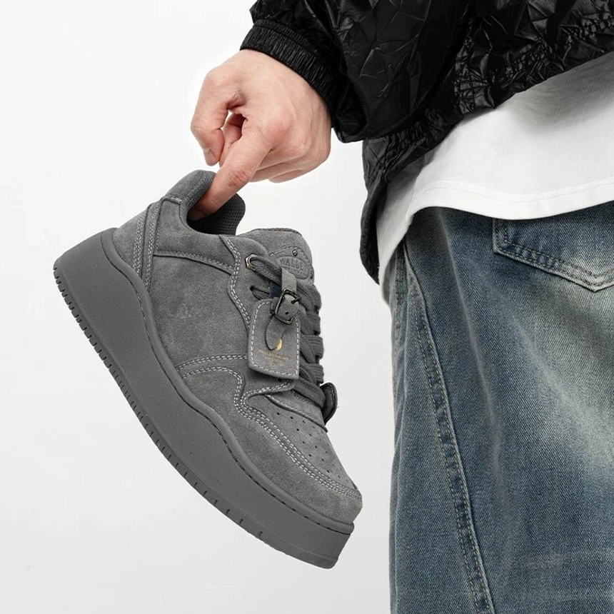 Angled close-up of grey suede-textured low-top platform skate sneakers with decorative tongue detail and chunky rubber outsole
