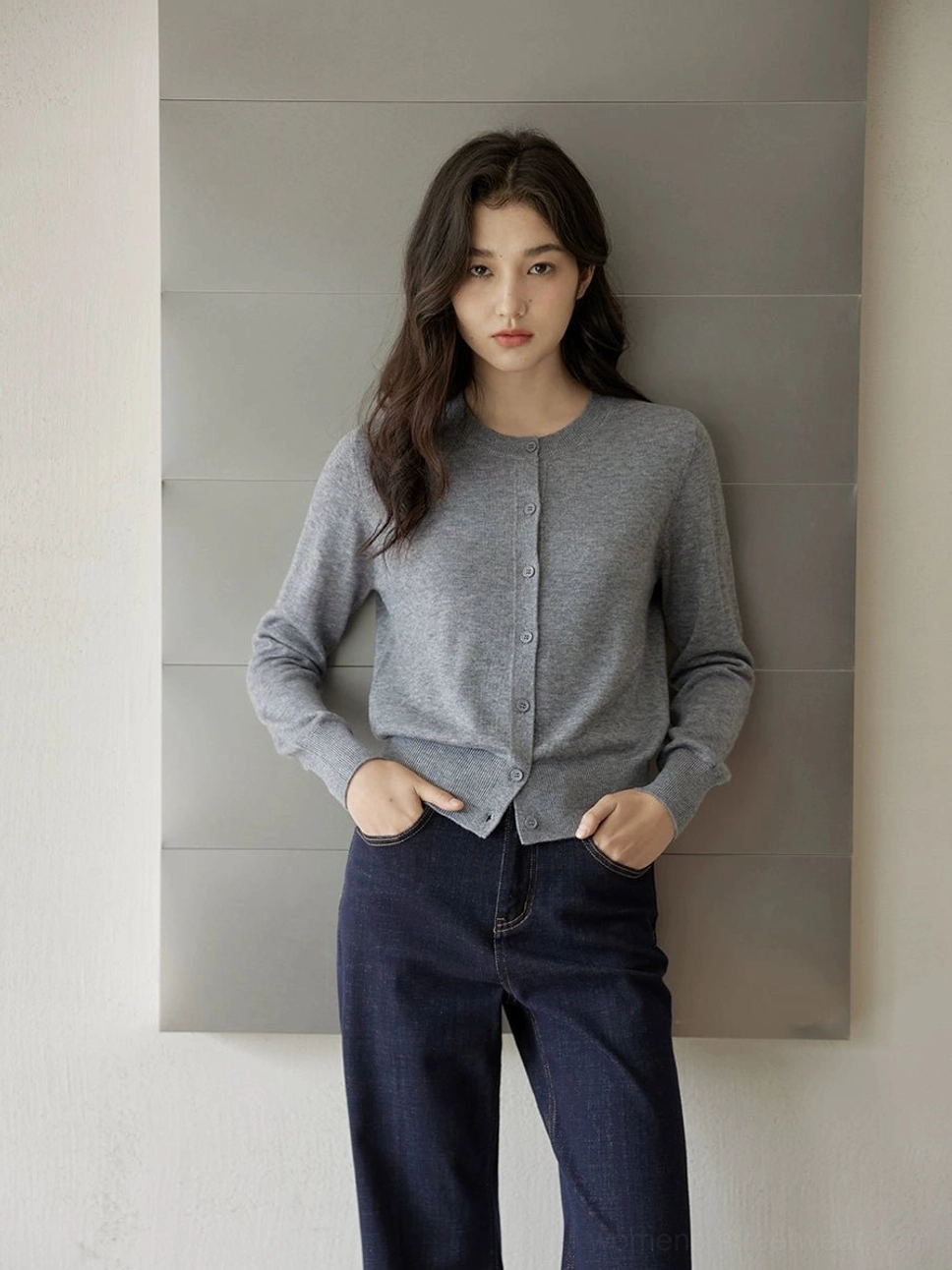 Grey women's crew neck button-front cardigan styled with dark wide-leg jeans in a minimalist indoor setting, showing the cropped fine-knit streetwear silhouette