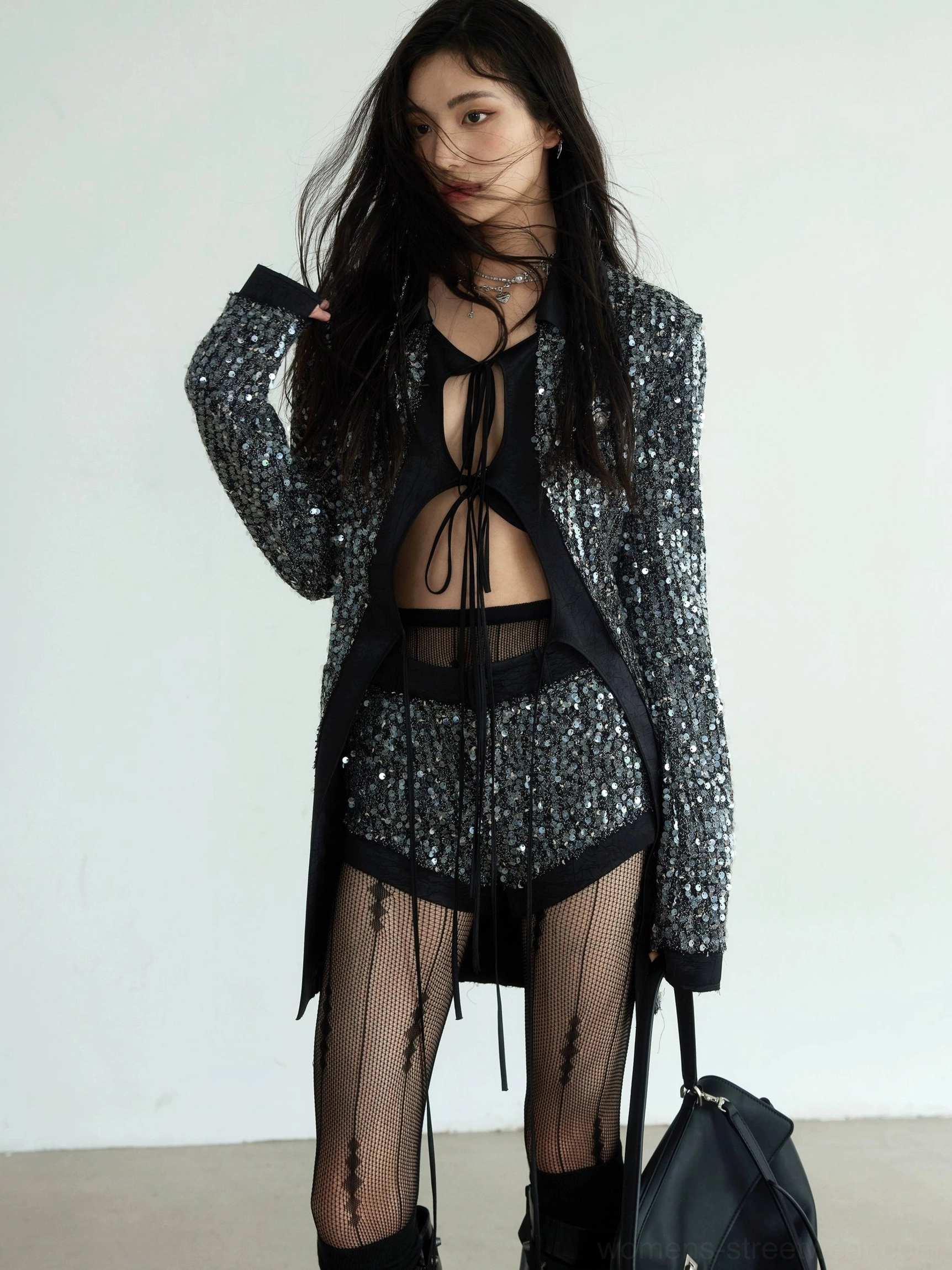 Front three-quarter view of a woman wearing a gunmetal silver sequin oversized blazer and matching low-rise shorts with black satin trim and striped fishnet tights