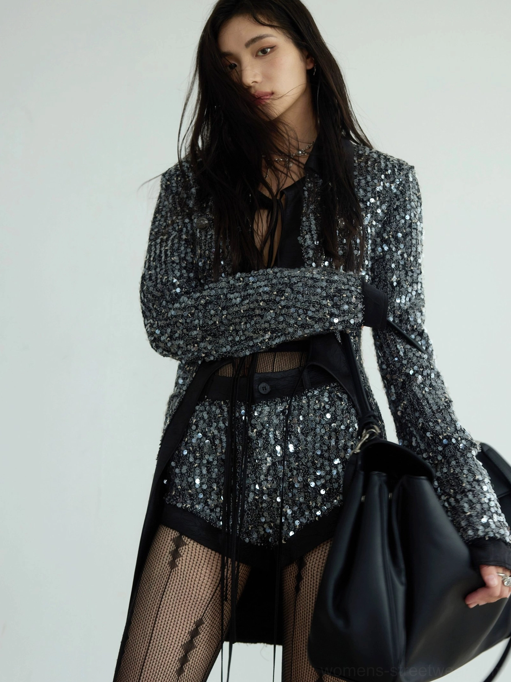 Side three-quarter view of a gunmetal silver sequin blazer and matching low-rise shorts with black waistband trim and oversized streetwear silhouette