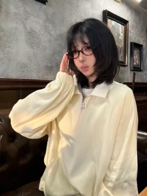 Cream apricot half-zip raglan polo pullover with contrast white collar and relaxed sleeves styled in a vintage indoor lounge