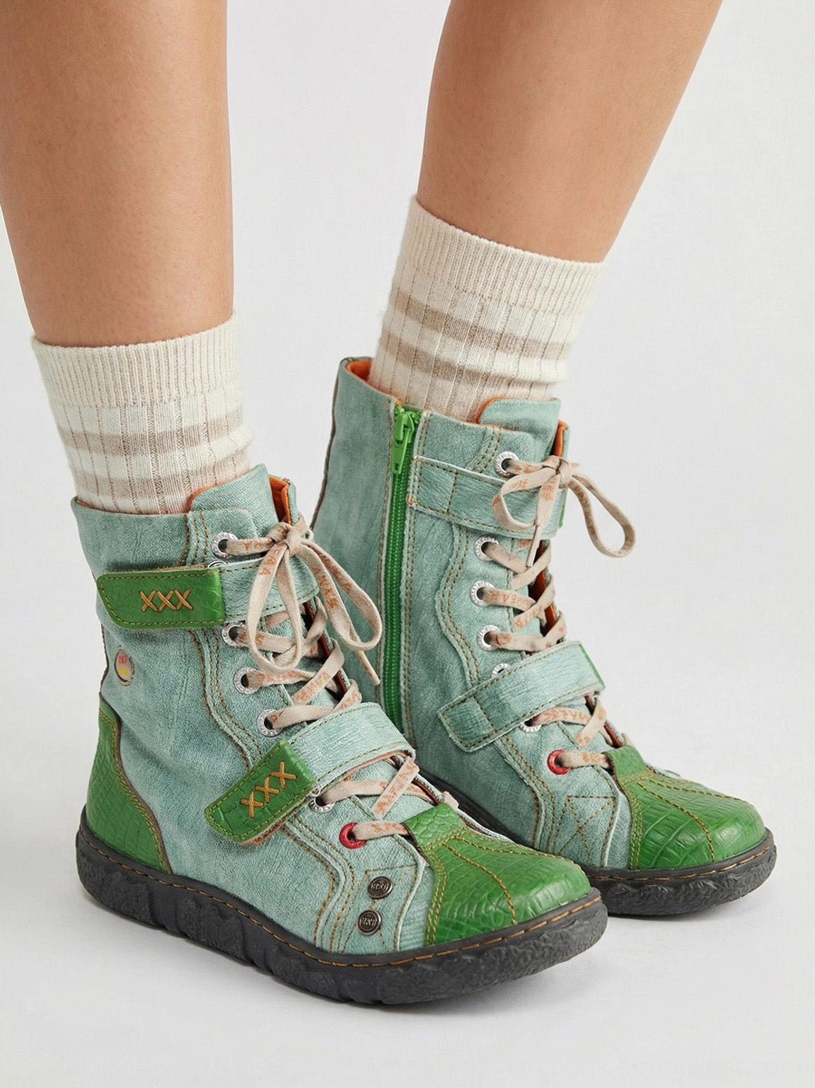 Model wearing green hand-stitched mid-calf streetwear boots with striped cream socks on white background