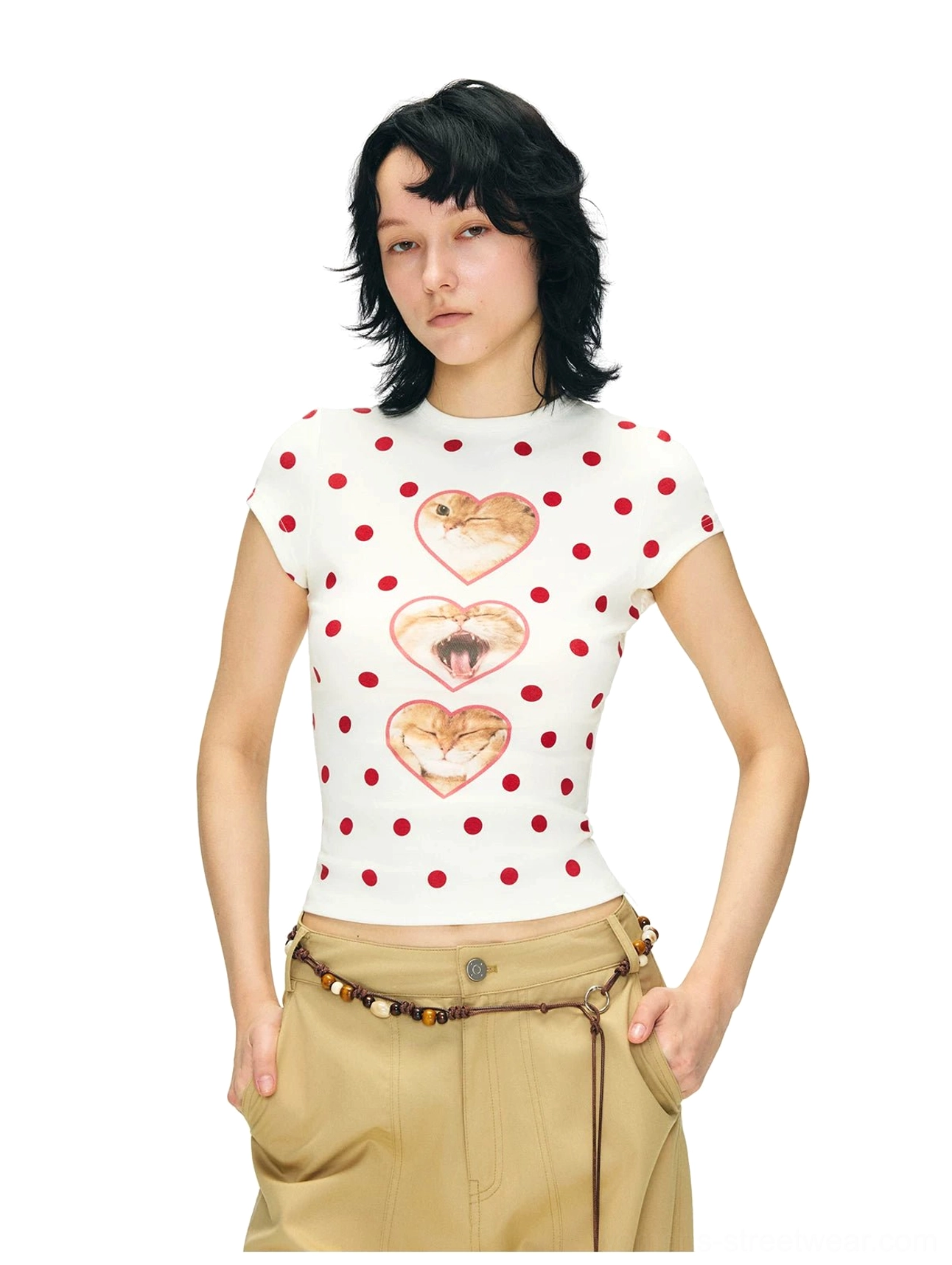 Close three-quarter view of a fitted cropped cat heart graphic tee with red polka dots styled with khaki trousers and a beaded belt