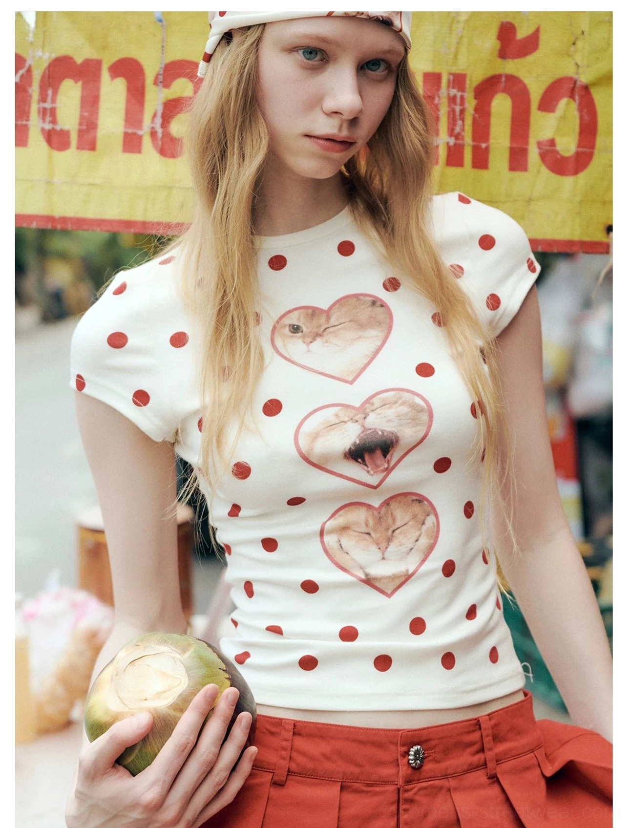 Model wearing an off-white heart cat polka dot Y2K streetwear T-shirt with red pleated shorts and matching headscarf at an outdoor street market
