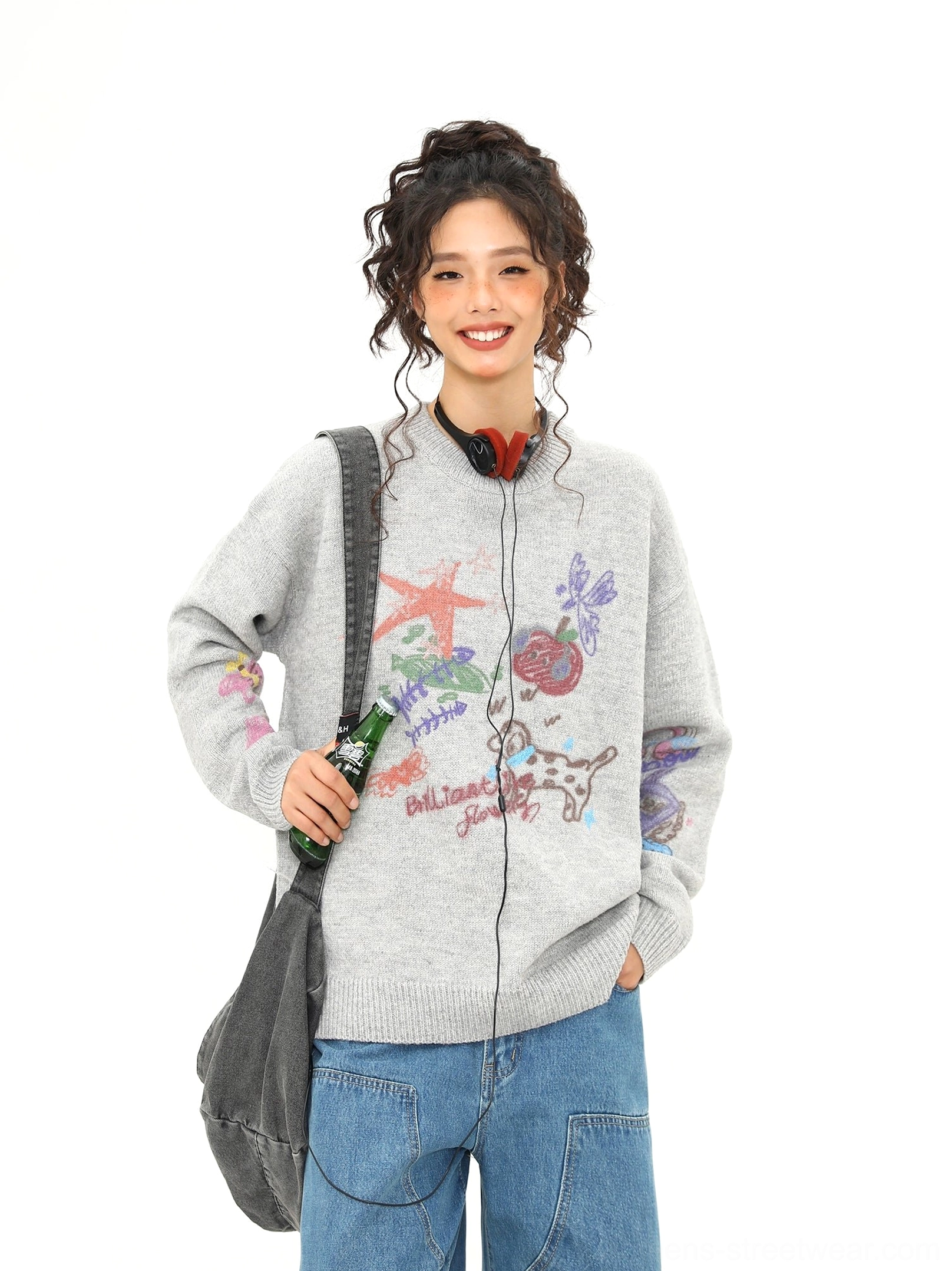 Smiling model wearing a loose heather gray puppy doodle knit sweater with colorful handwritten style graphics
