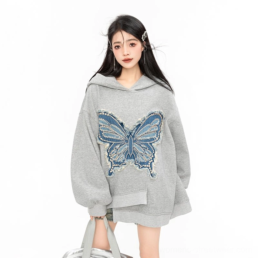 Upper body close-up of heather grey oversized butterfly hoodie featuring a frayed blue denim butterfly chest patch and loose sleeves