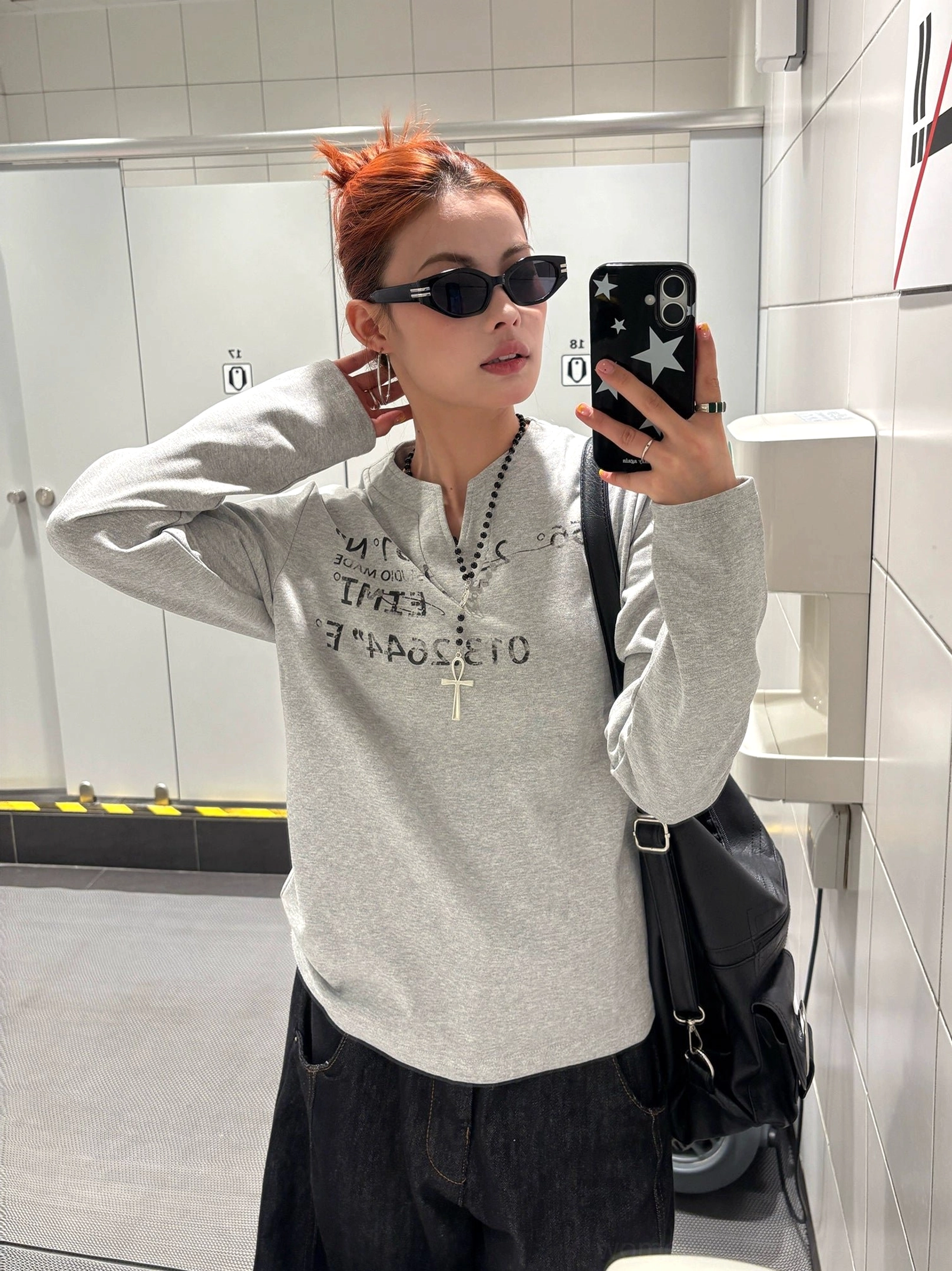 Front close-up view of a woman wearing a heather grey printed Henley top with reversed text graphic and soft long sleeves