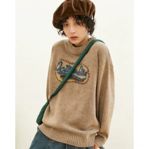 Heathered oatmeal beige gray oversized crewneck knit sweater with ribbed trims and dimensional embroidered chest patch styled with wide-leg jeans