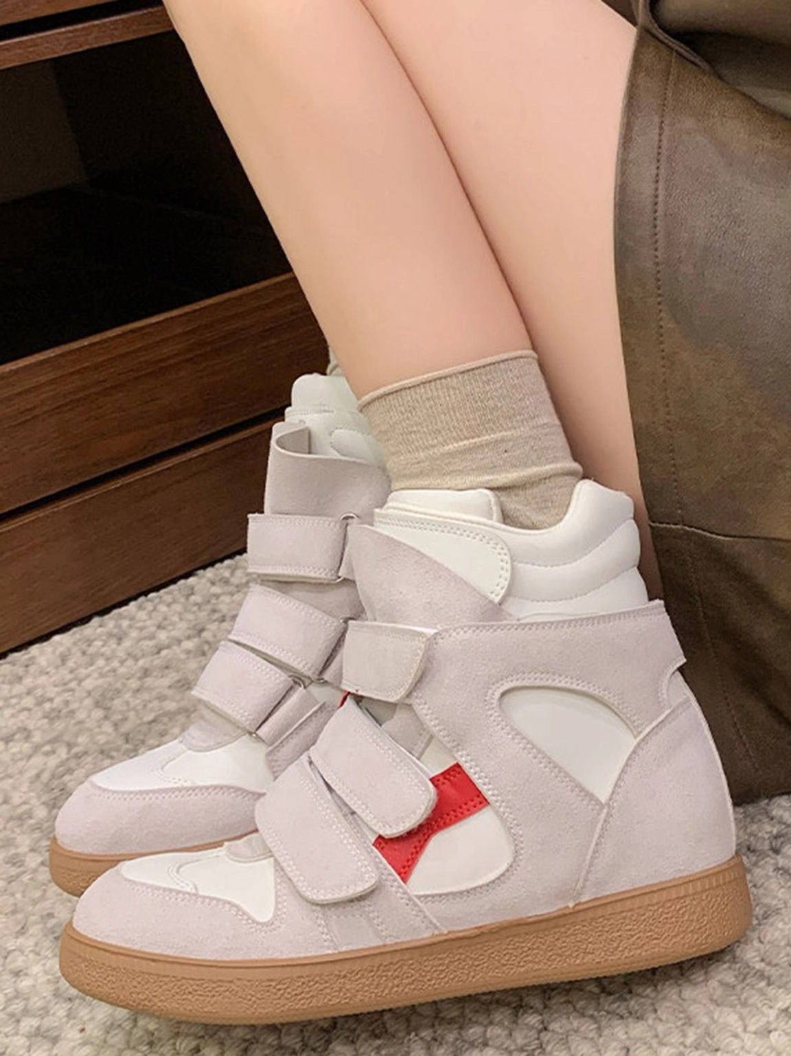 Rear three-quarter view of women's hidden-wedge high-top sneakers with light gray suede upper, red side accent, dual Velcro straps, and gum sole